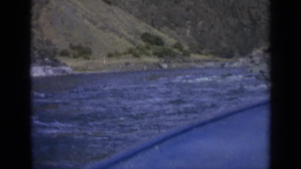 Final 8mm frame showing choppy Washington river water, a low shoreline, sparse vegetation, and the boat edge in foreground.