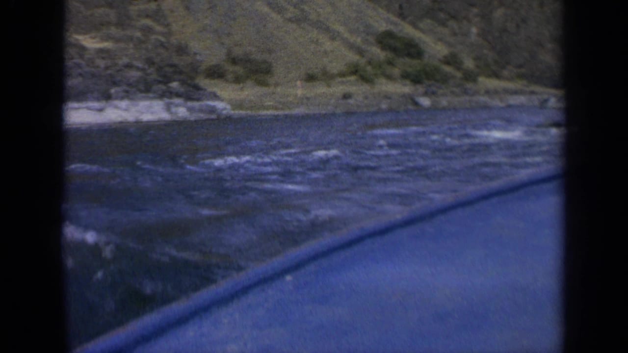 Choppy water beside a blue boat edge with a rocky grassy shoreline beyond.