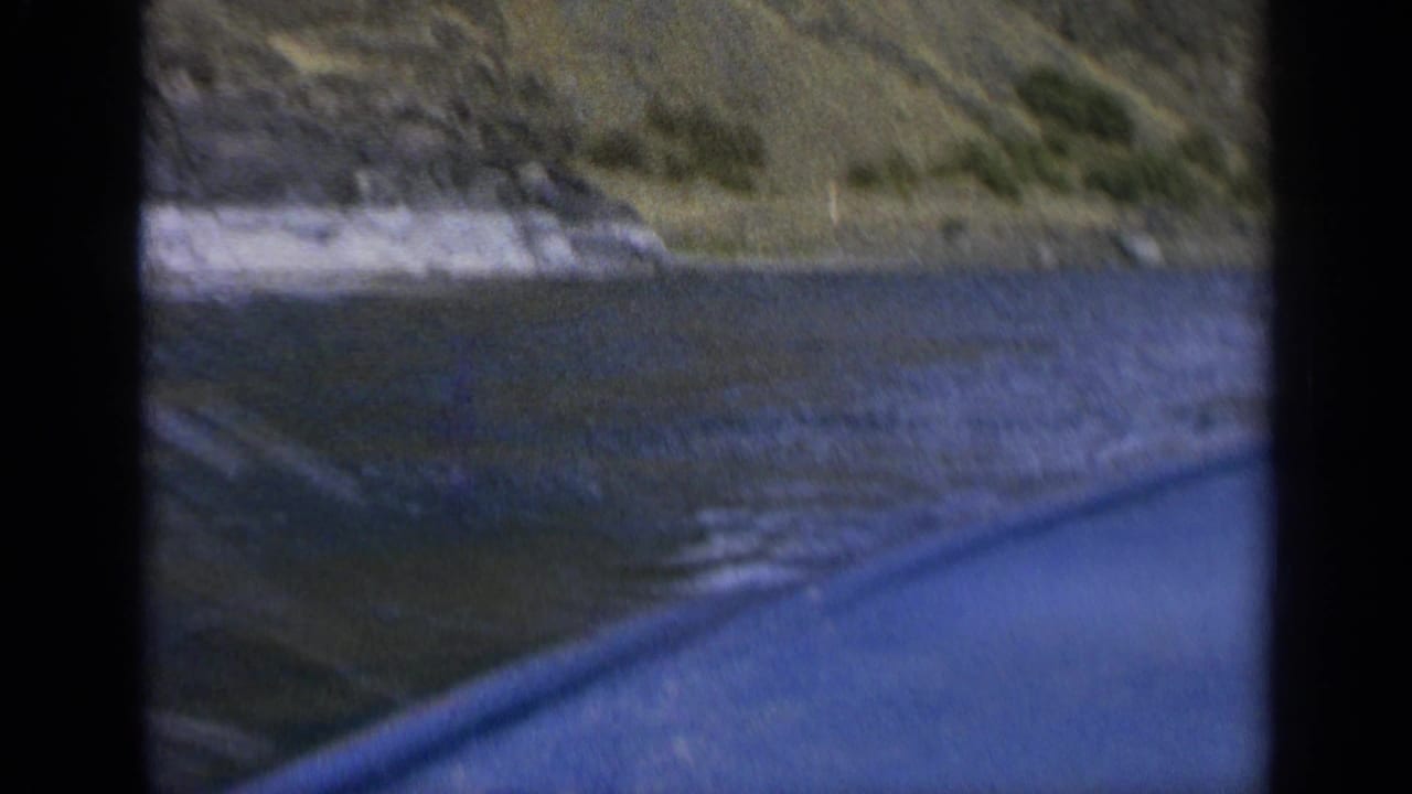 Soft 8mm frame from the moving boat, with water in the foreground and a rocky Washington shoreline beyond.