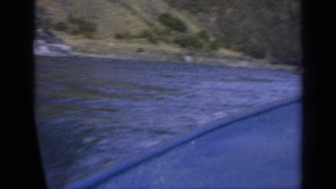 1963 Washington 8mm frame showing the boat passing over choppy water near a low grassy and rocky bank.