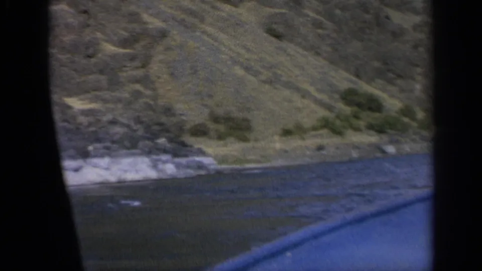 River shoreline in Washington, 1963, with rocky bank and hillside seen from a moving boat on 8mm film.