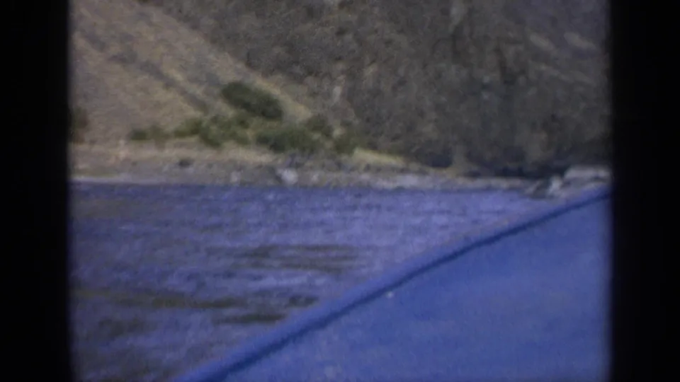 Washington river scenery from a moving boat, with blue water foreground and rugged hillside beyond.