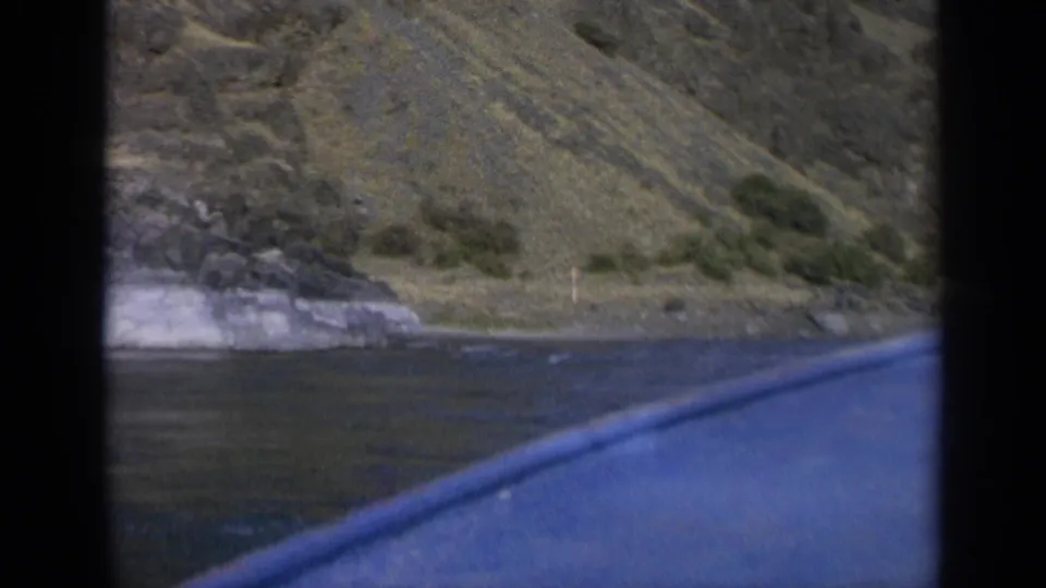 A moving boat view shows rippled water, a pale rocky outcrop, and a sloping Washington hillside.
