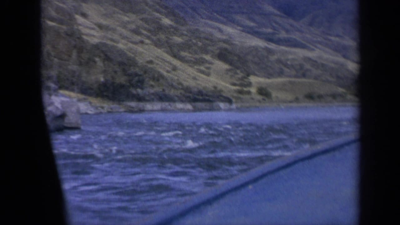 Moving 8mm boat view in Washington, with whitecapped lake water and a rugged mountainside framed by dark window edges.
