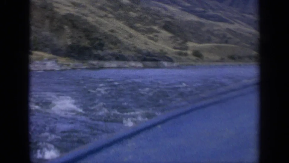 1963 Washington 8mm view of a rushing river beside dry hills, filmed through a dark vehicle window frame.