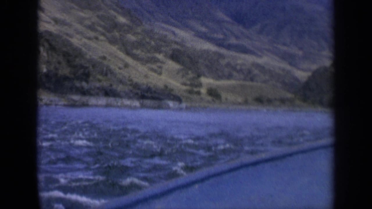 River current, hillside, and dark window divider in a moving landscape view.