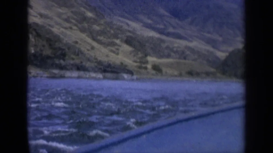 Blue-tinted 8mm frame showing Washington river current and hillside through a vertical window divider.
