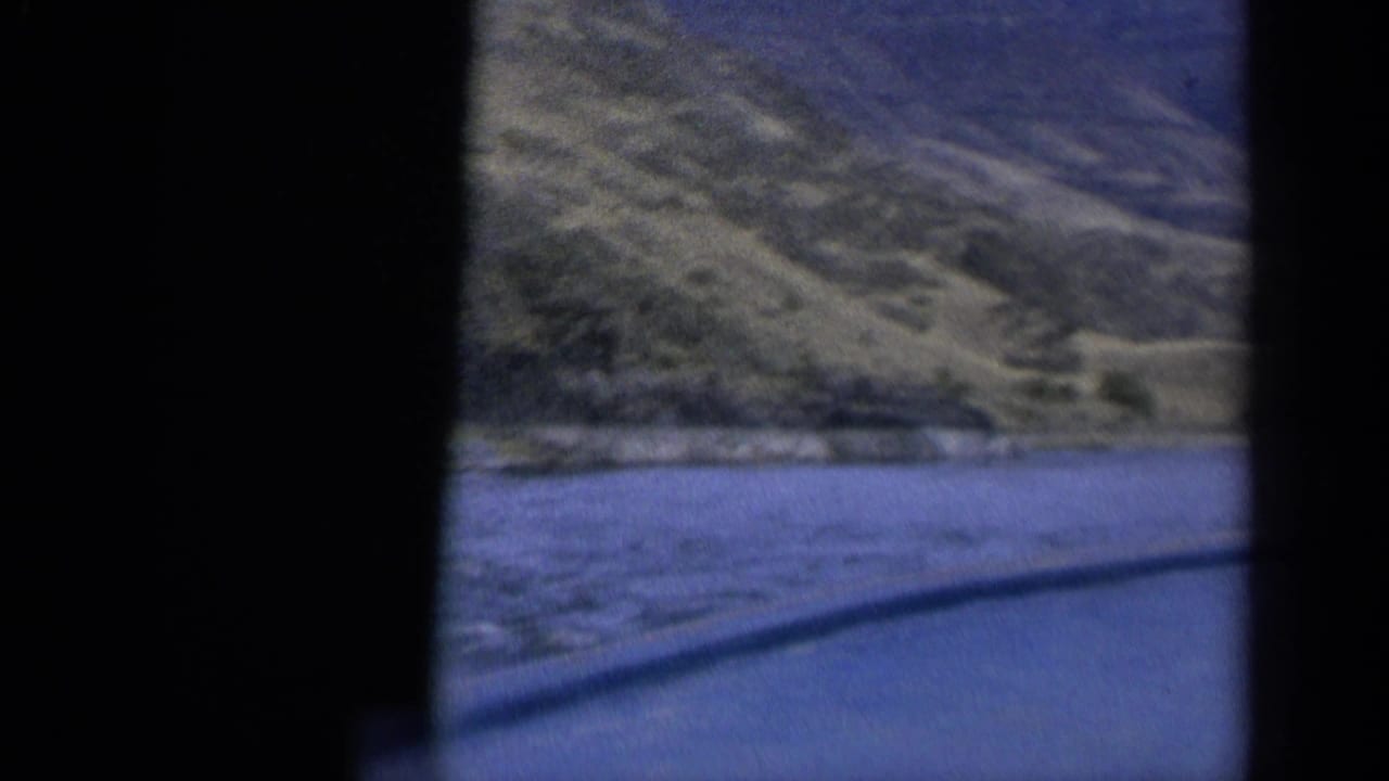 1963 Washington travel frame with hillside above a river edge and a diagonal window or vehicle line in front.