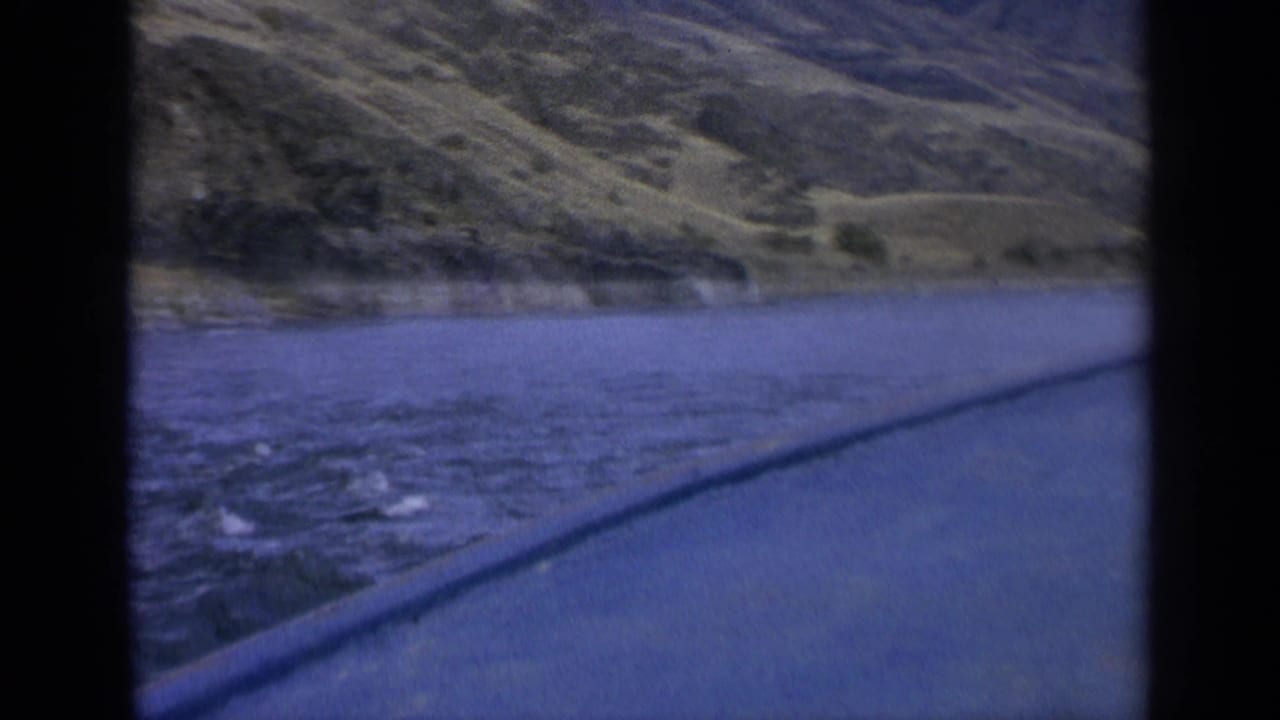 Lake surface and green mountain slope seen from a moving vehicle perspective.