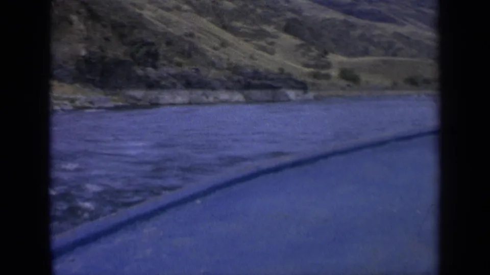 1963 Washington home-movie frame showing rippled blue water, hillside shoreline, and the foreground edge of a moving viewpoint.