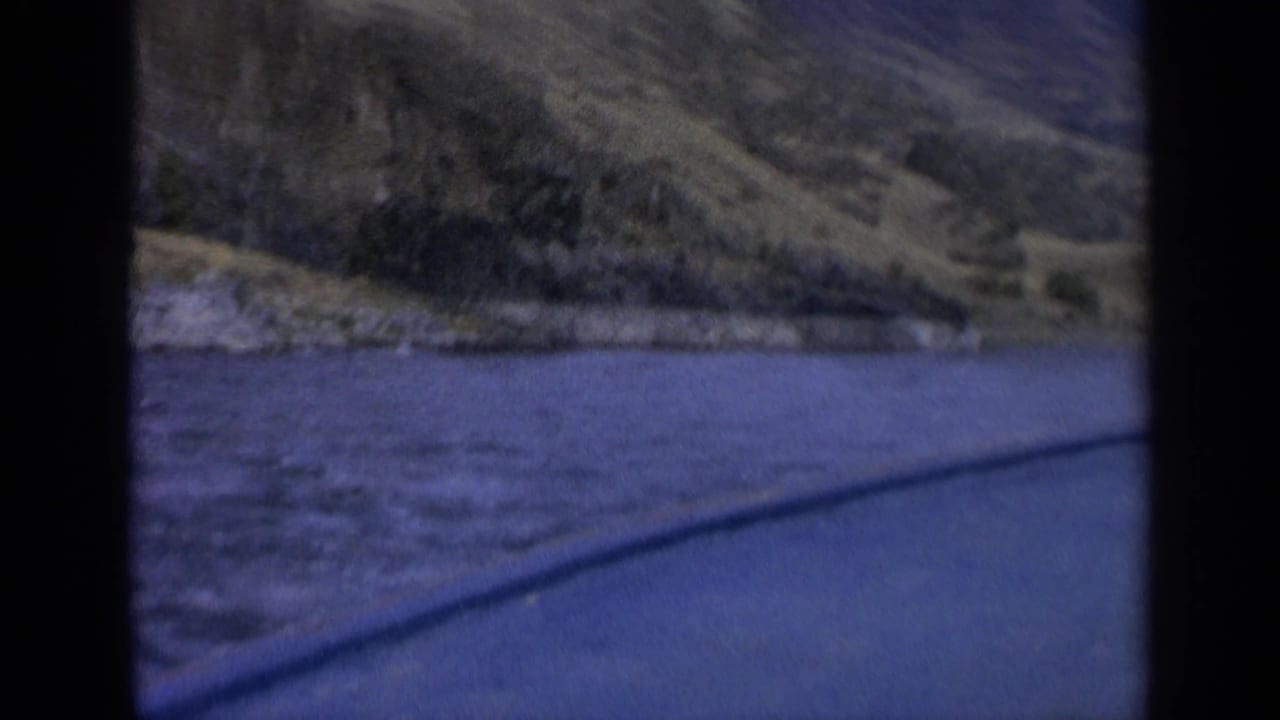 1963 Washington 8mm frame showing a blue river beside dry rolling hills, seen through dark film-frame borders.