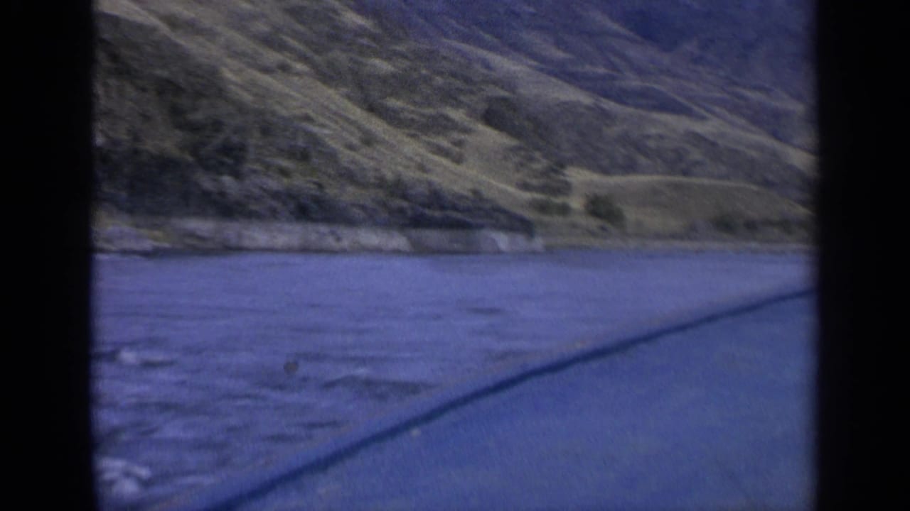 River and hillside shoreline seen through vertical dark film-frame bands.
