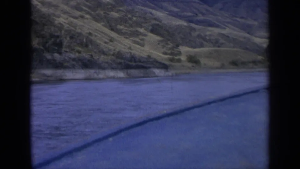 1963 Washington frame showing blue river water below a dry hillside, divided by a dark film-frame border.