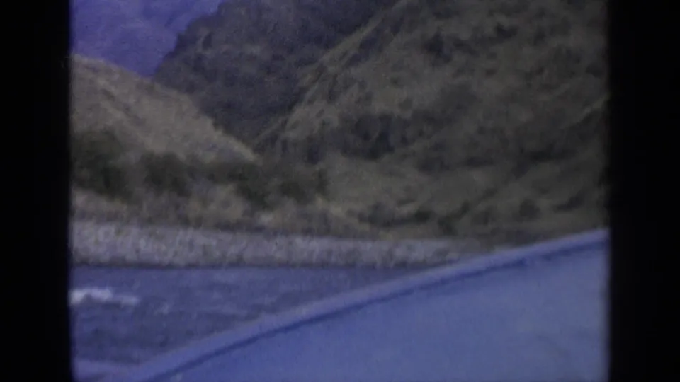 Home-movie frame from a boat on a Washington river, with water in the foreground and steep dry hills rising beyond the bank.
