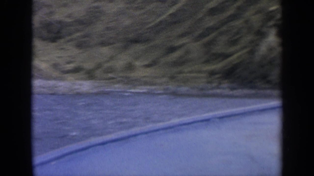 Roadside river and mountain slope seen through dark car-window framing.