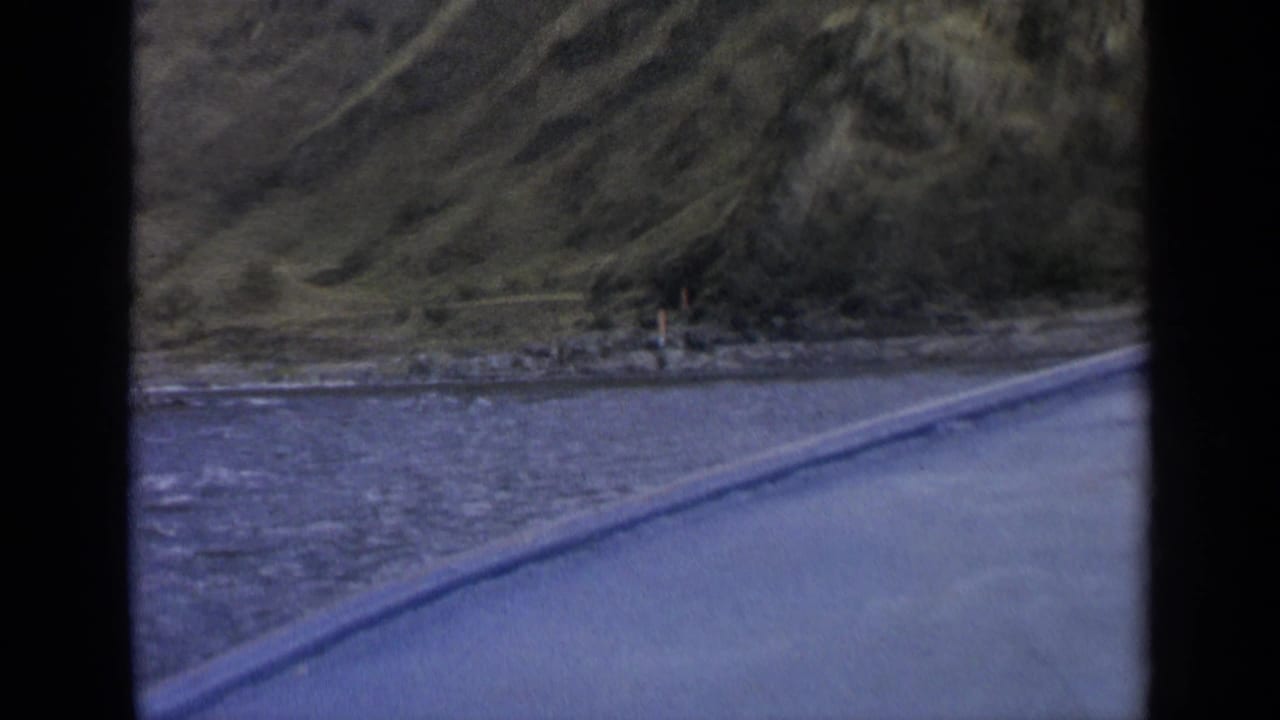 Car-window view of a road following water below rugged Washington mountain slopes in 1963 home-movie footage.