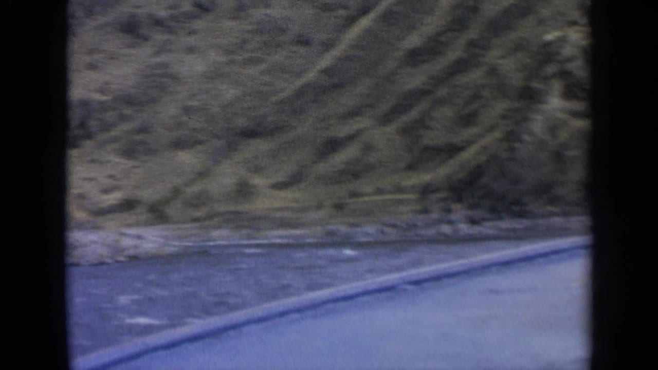 Motion-softened 8mm frame showing river, road edge, and mountain slope during a 1963 Washington scenic drive.
