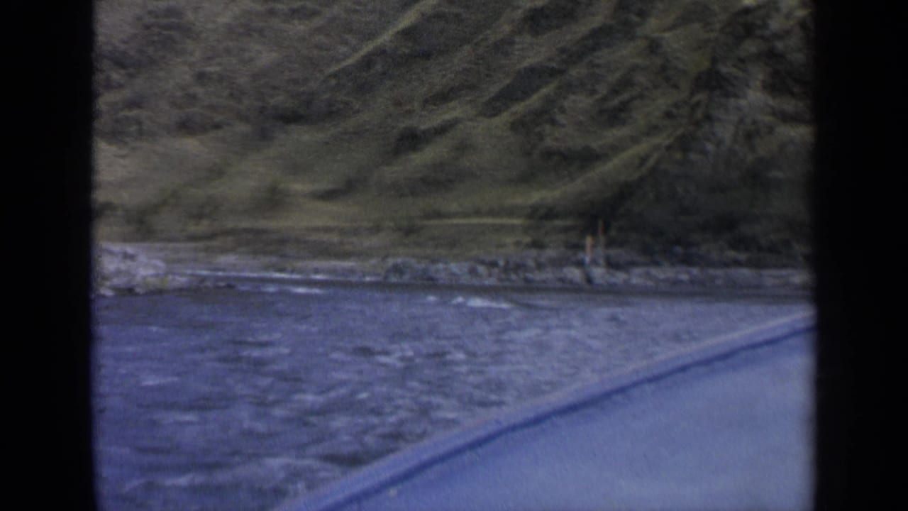 Roadside river view with hillside and a small distant figure near the bank.