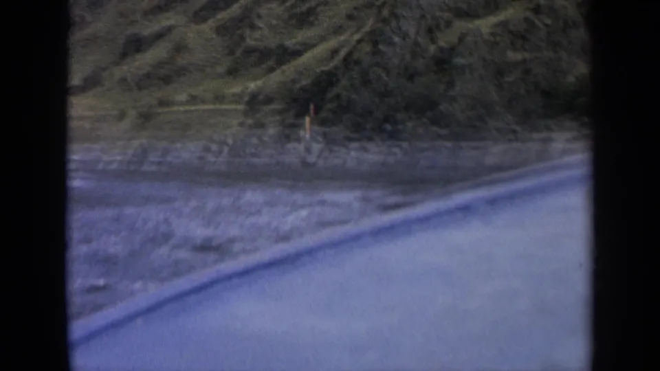 1963 Washington 8mm frame showing a slightly blurred boat-level view of shoreline water, rocks, and green hills.