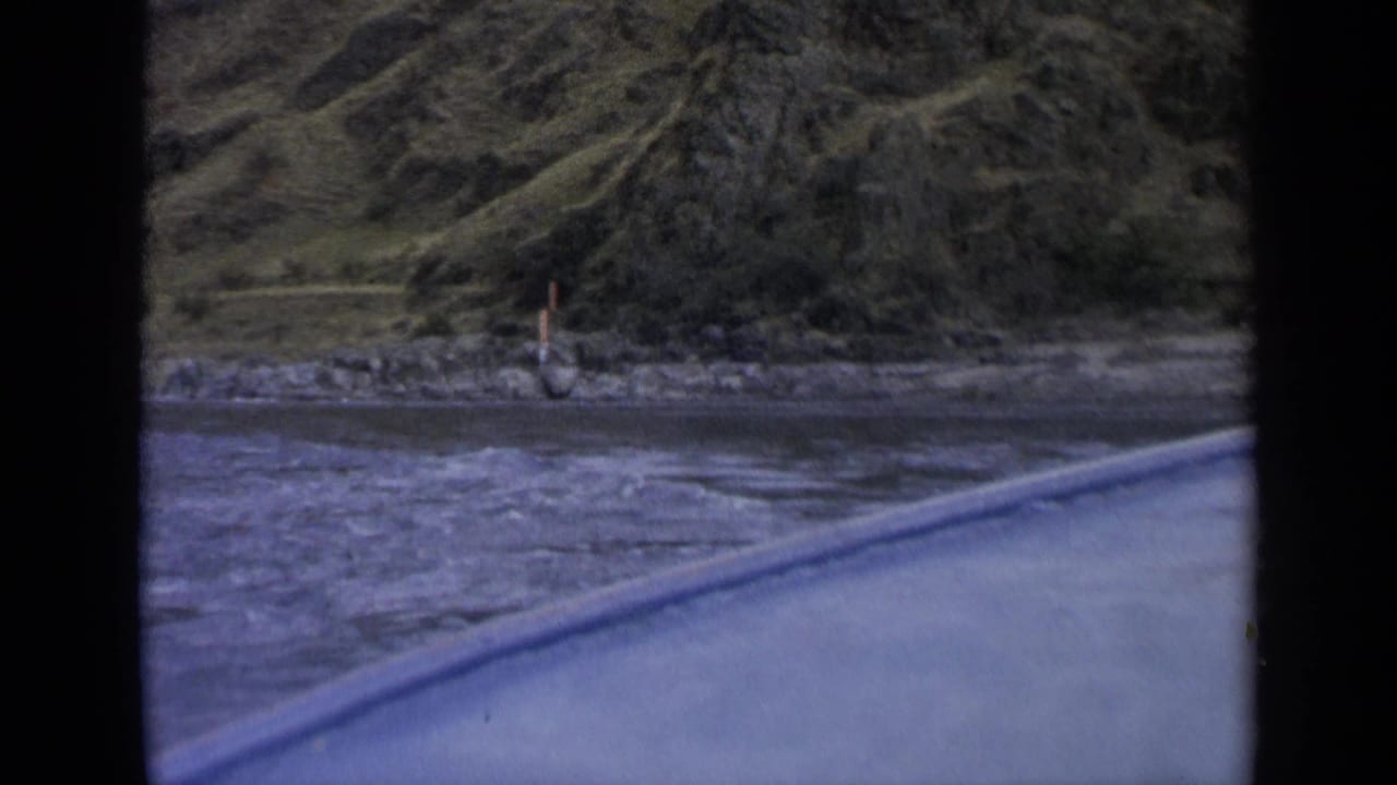 1963 Washington 8mm view of a river and shoreline passing by, with dark frame borders and a blue vehicle or boat edge in front.