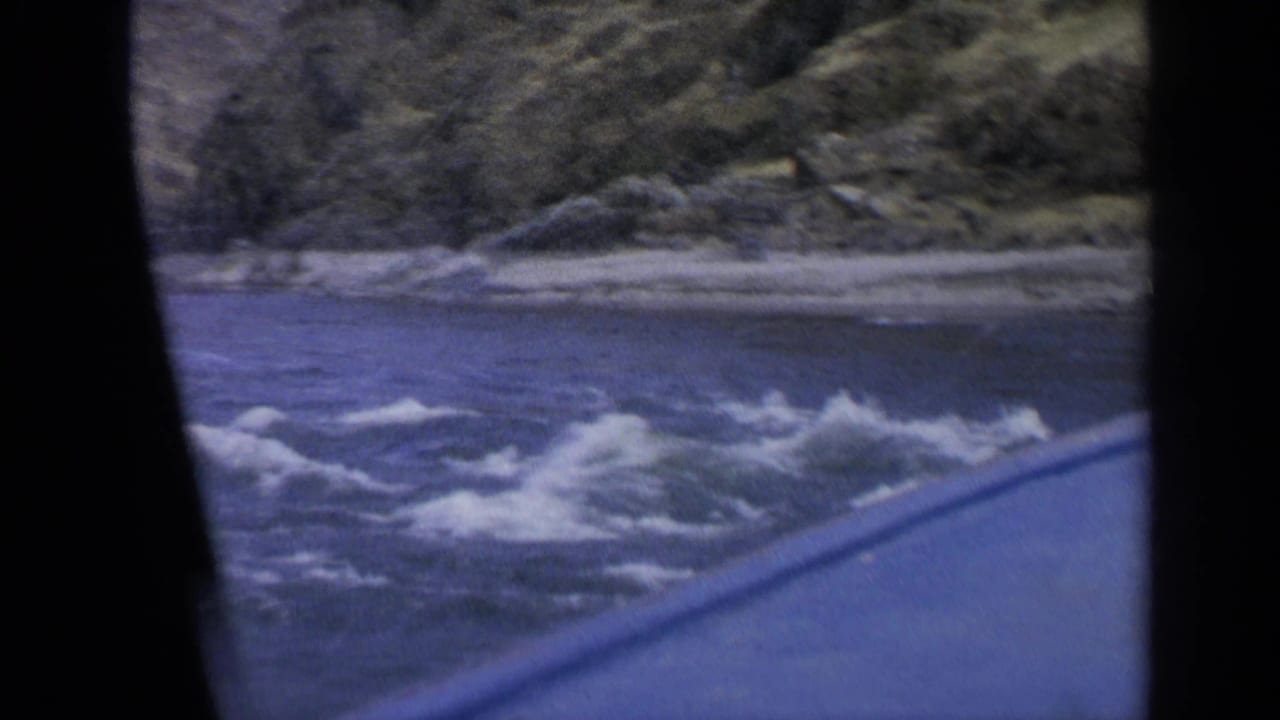 A 1963 Washington home-movie frame catches foaming rapids and a low rocky bank from a moving vantage point.