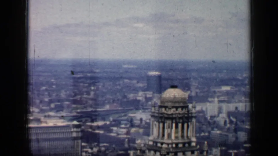 1957 8mm frame of Chicago from above, with a domed tower, broad building rooflines, and hazy distance.