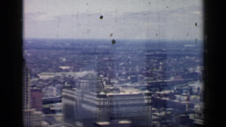 1957 Chicago downtown skyline viewed from above through a window, with tall buildings and dense city blocks softened by 8mm film texture.