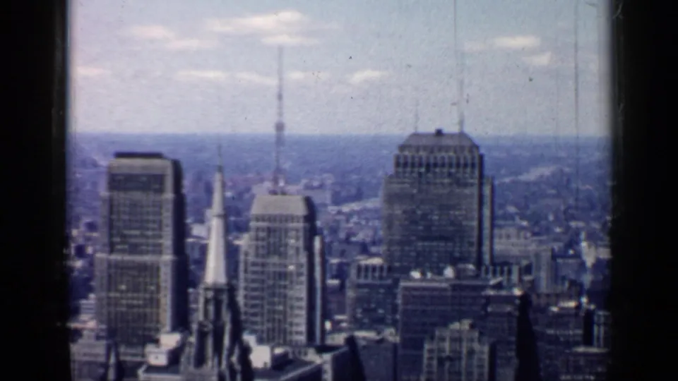 High view across 1957 Chicago with clustered office towers, church steeples, a tall rectangular building, and soft archival color shift.