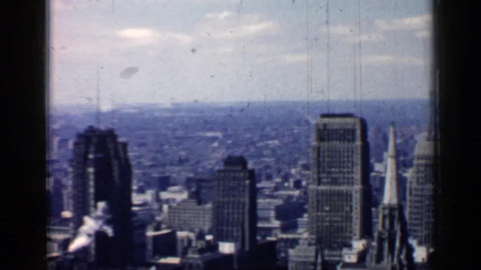 Chicago skyline view showing a dark tower, church steeple, rectangular office building, low rooftops, and a hazy mid-century city background.