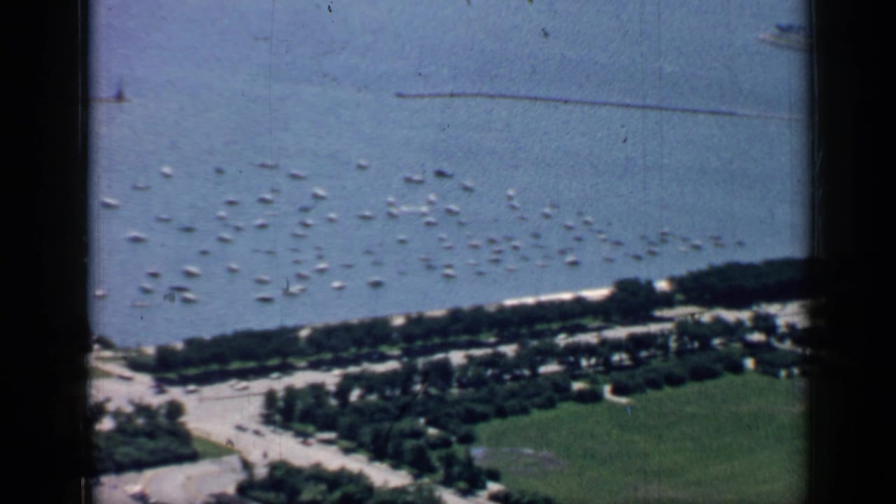 Aerial view of many small boats anchored near a shoreline and long pier.