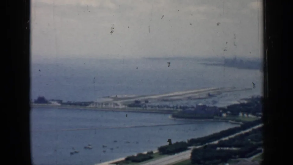 1957 Chicago lakefront scene with a long pier or causeway, boats on the water, shoreline roads, and distant buildings.