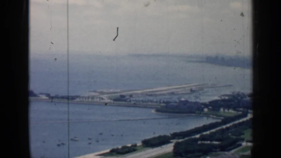 Wide 1957 Chicago lakefront view with small boats on the water, shoreline roads, trees, a long pier, and distant buildings.