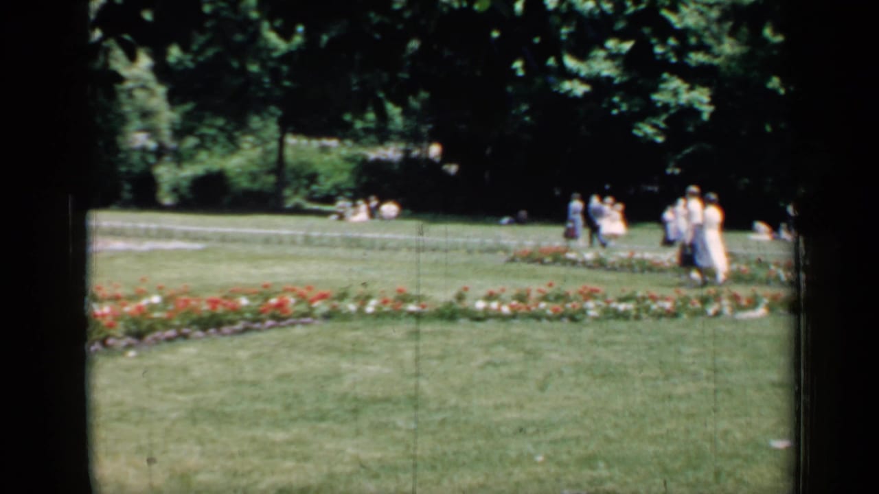 Distant people walking near flower beds and lawns in a shaded park view.