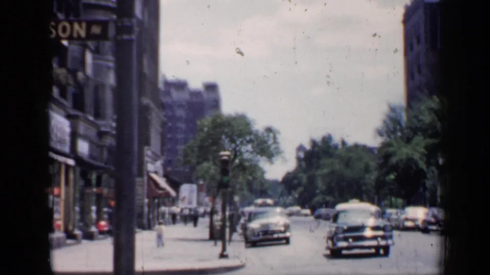 Chicago street corner in 1957 with pedestrians on the sidewalk, mid-century cars in the road, and storefront signage along brick buildings.