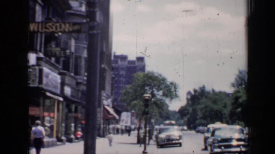 1957 Chicago view near a visible Wilson Ave sign, with classic cars, pedestrians, storefronts, trees, and streetlights.