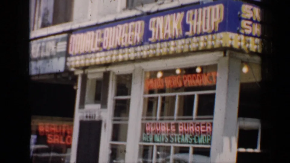1957 Chicago storefront view with the Double Burger Snak Shop sign, bright marquee bulbs, and food advertising in the windows.