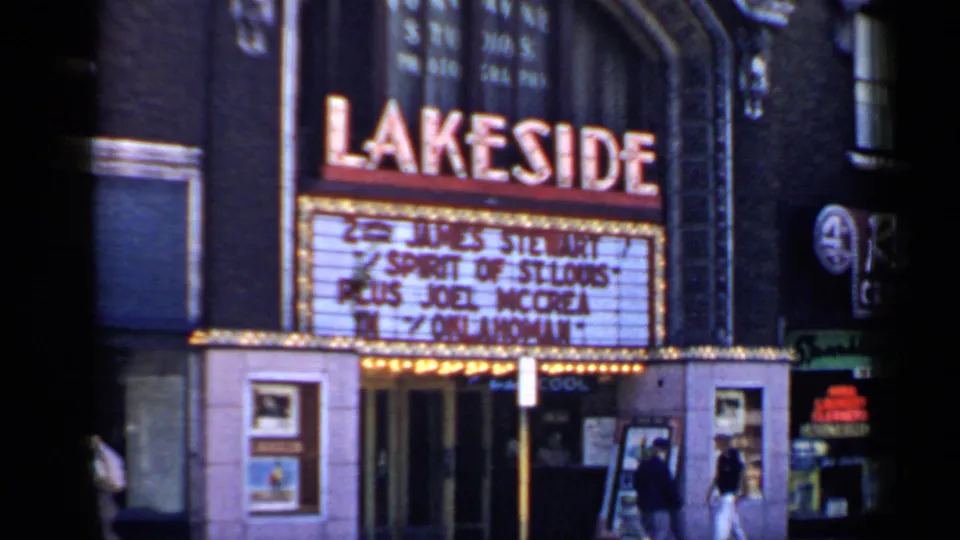 Handheld 8mm view of the Lakeside Theatre marquee, entrance doors, display cases, and pedestrians on the sidewalk.