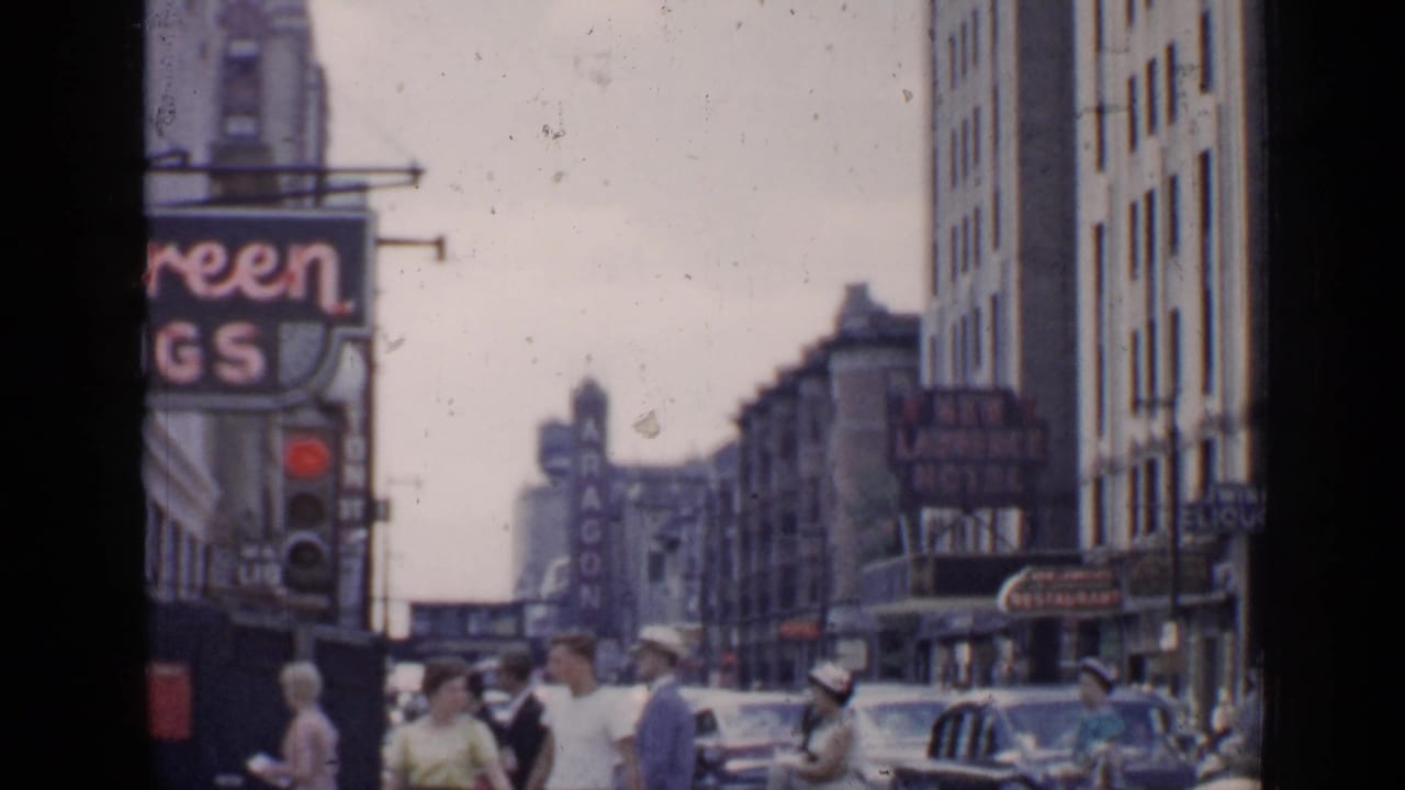 Busy Chicago street with pedestrians, cars, tall buildings, and theater-district signage.