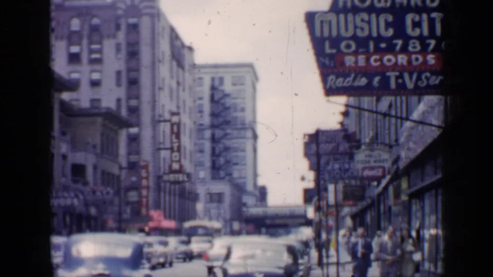 1957 Chicago street view with the Wilton Hotel sign, Howard Music City storefront sign, vintage cars, and pedestrians along the sidewalk.