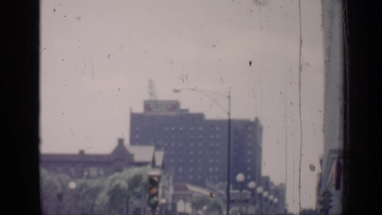 Soft street view through a dusty window with a distant high-rise and traffic signal.