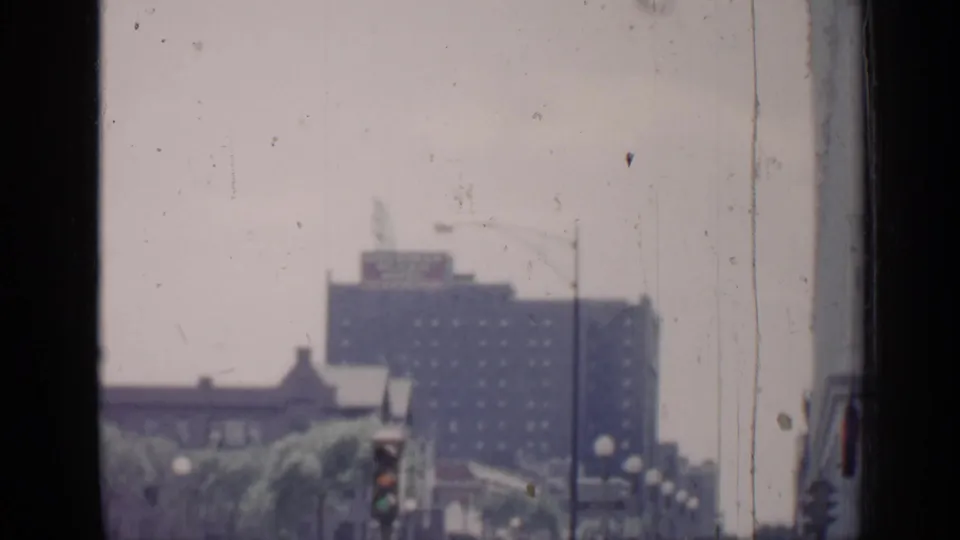 1957 Chicago home-movie frame showing a blurred street view through glass, with a distant high-rise, traffic signal, and film dust.