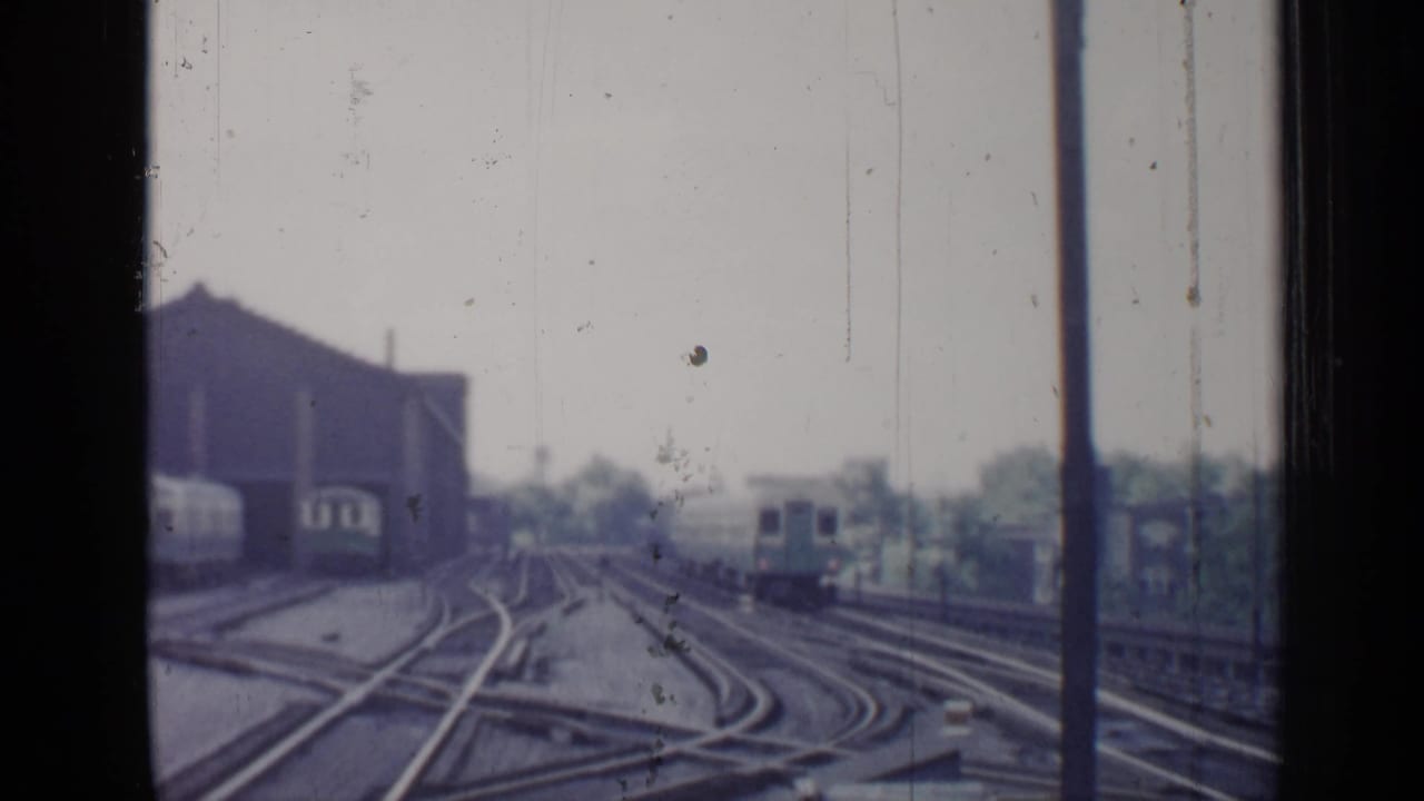 Rail yard tracks and switches seen through a window, with buildings in the background.