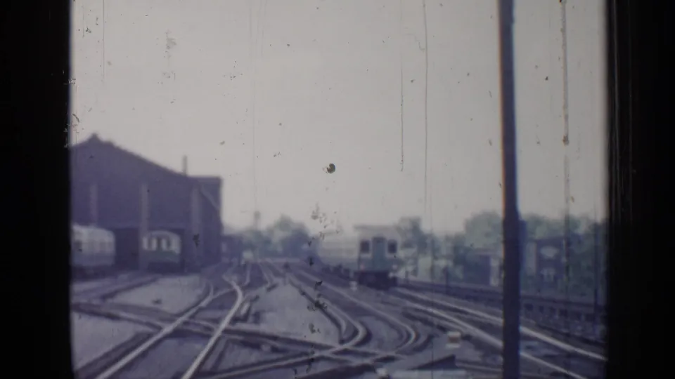 1958 Chicago rail yard view with multiple tracks, switches, industrial buildings, and window framing in soft 8mm color.