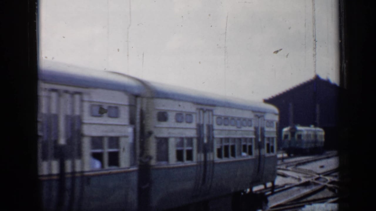 Commuter railcars beside station tracks with dark film frame edges.