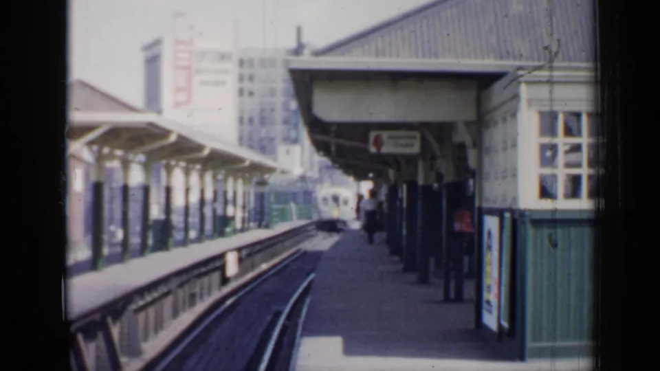 1958 Chicago commuter station view with covered platform, curving tracks, distant train, signage, and city buildings beyond.