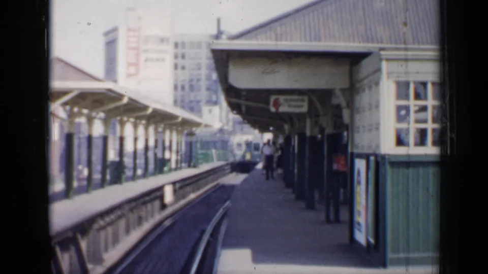1958 Chicago 8mm view down a commuter platform toward an approaching train, with passengers and station architecture visible.