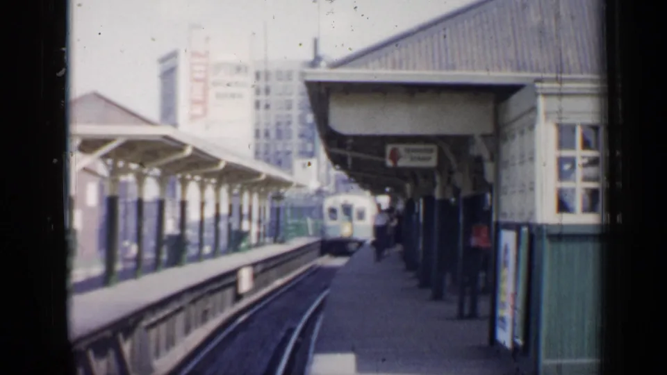 1958 Chicago station scene showing a commuter train near the platform, passengers, signage, and a green-and-white building.