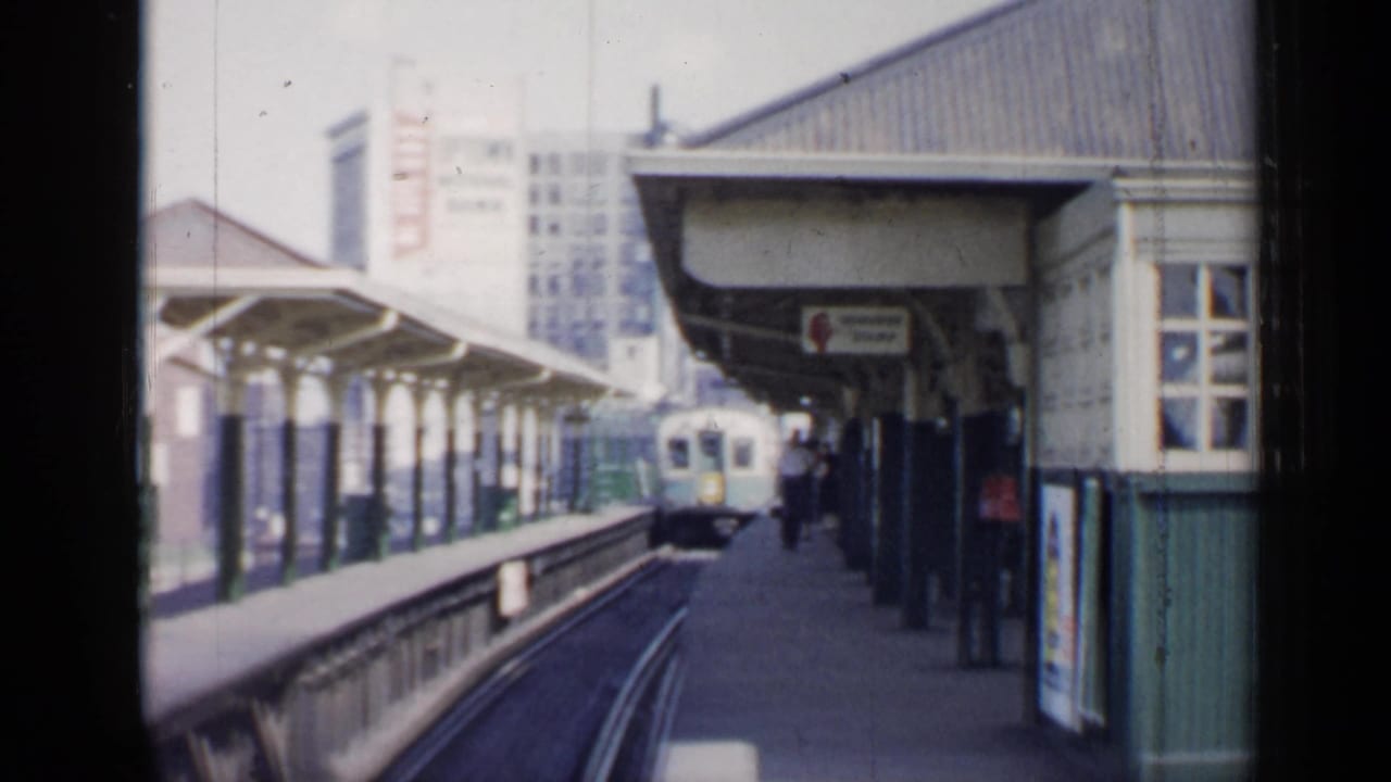 Elevated train approaches a covered station platform with passengers waiting.