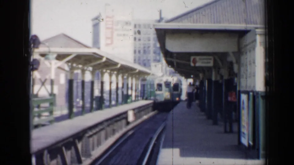 The elevated train nears the platform in Chicago, framed by station canopies, track curves, columns, and distant buildings.
