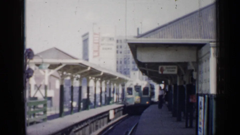 A 1958 Chicago elevated train enters the station area, with covered platforms, trackwork, passengers, and city buildings in view.